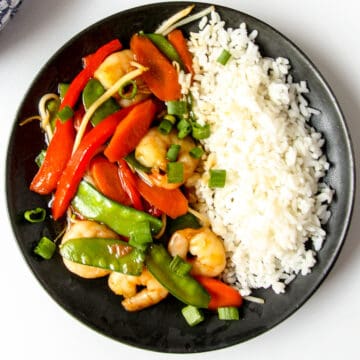 Shrimp chop suey and rice on a black plate.