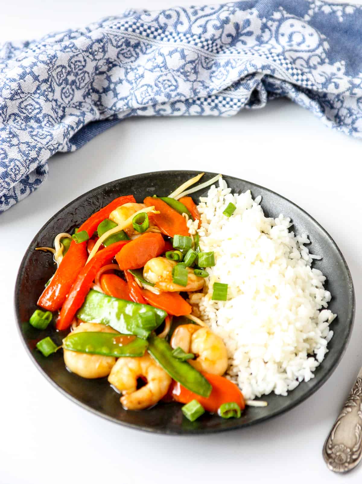 Chop suey and rice on a black plate with a silver fork and blue and white napkin.