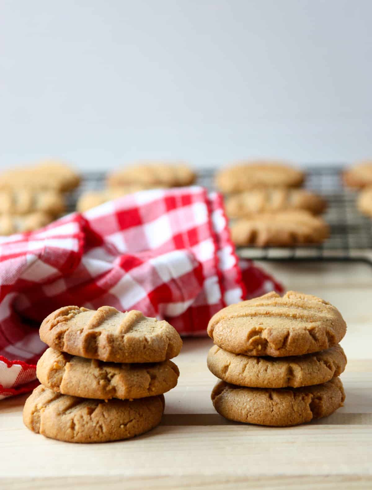 Two stacks of three peanut butter cookies on a wooden table beside a red and white napkin.