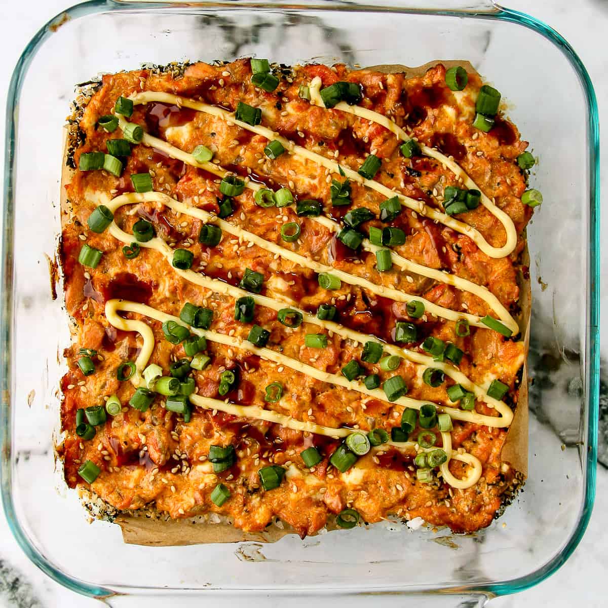 Salmon Sushi Bake topped with green onion slices in a glass baking dish.