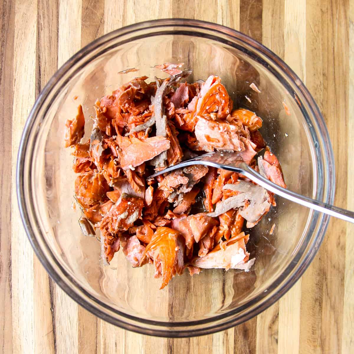 Pieces of cooked salmon in a glass bowl with a fork.