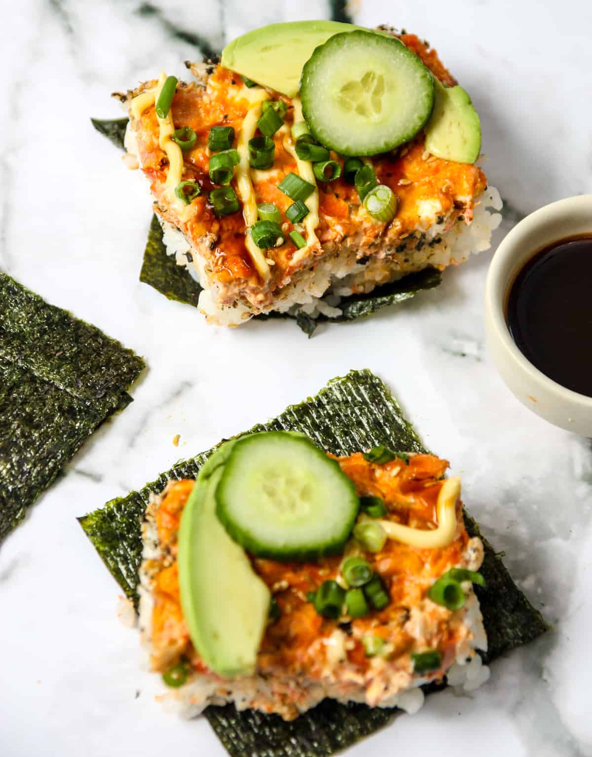 Two nori sheets topped with slice of sushi bake.