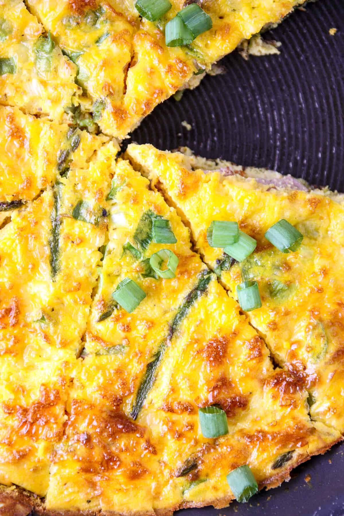 Frittata in a skillet, cut into wedges with one slice removed.
