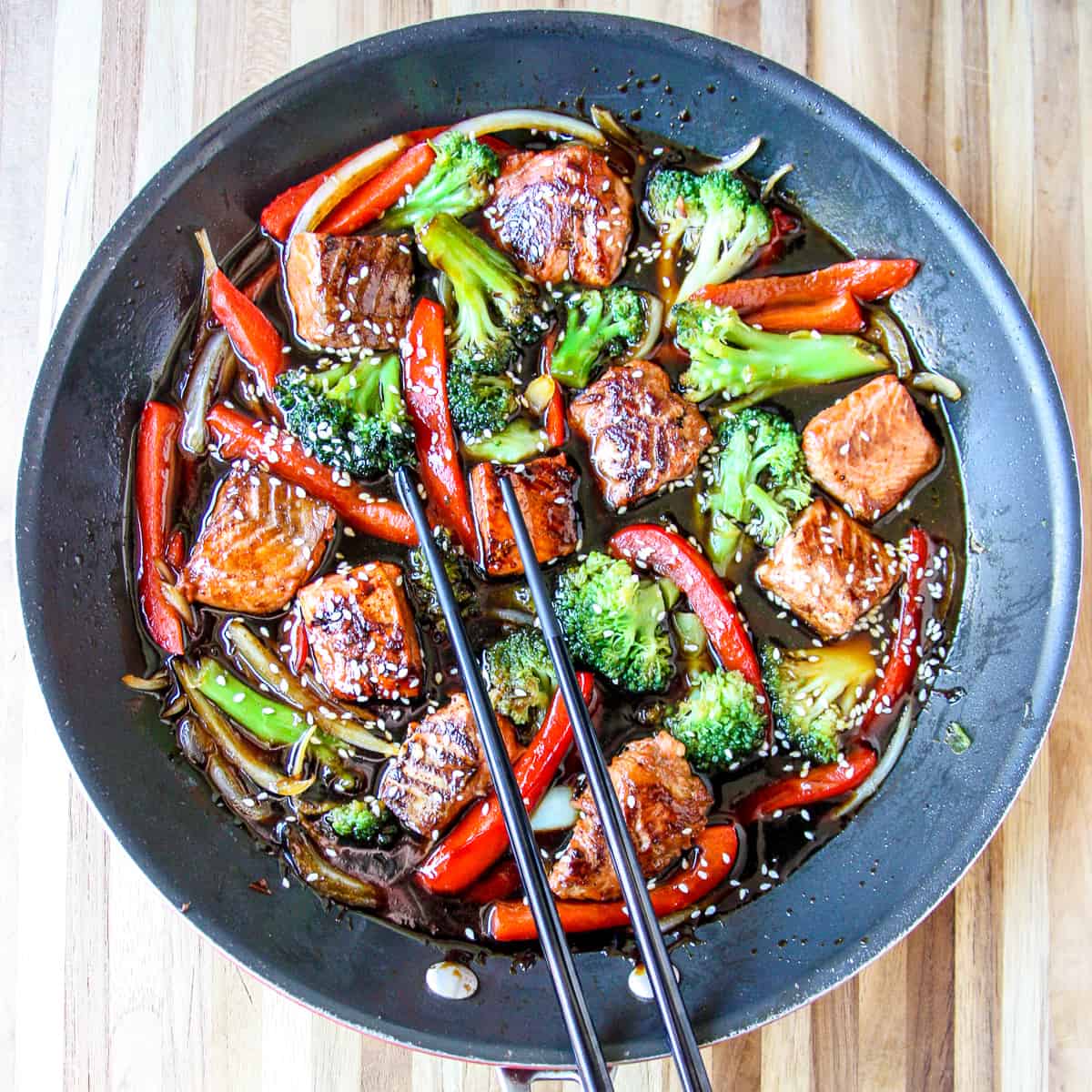 Teriyaki salmon stir fry in a black skillet with black chopsticks.