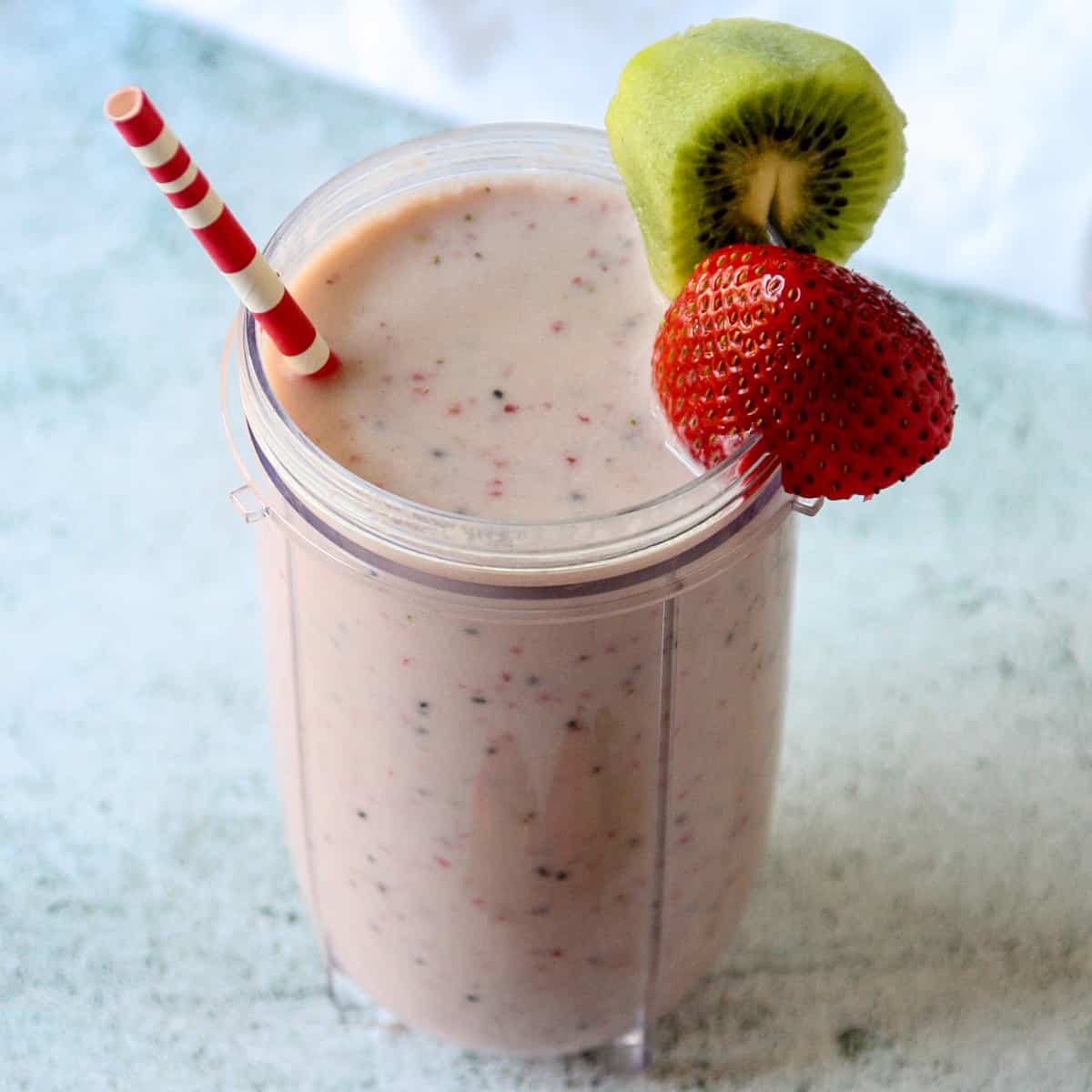Kiwi quencher tropical smoothie in a tall glass with a pink and white straw.