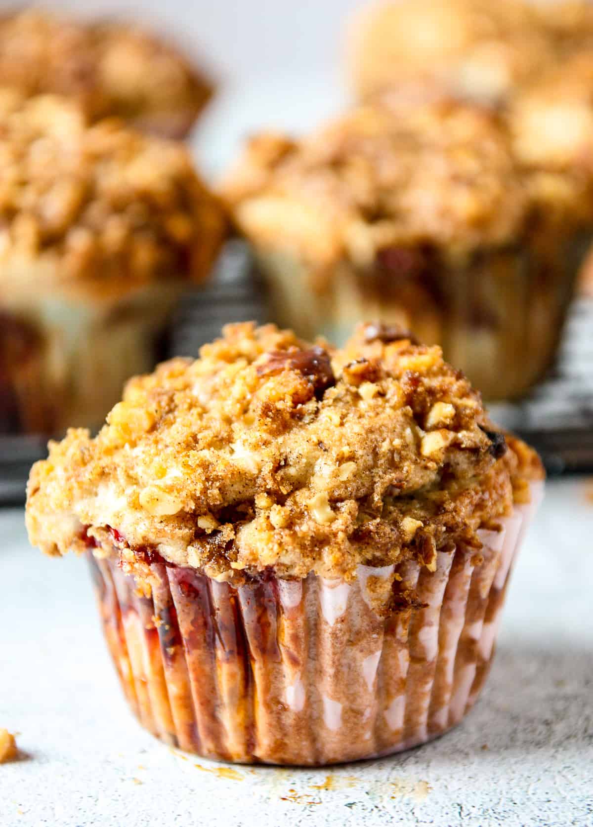 A streusel topped strawberry rhubarb muffin on a stone counter top.