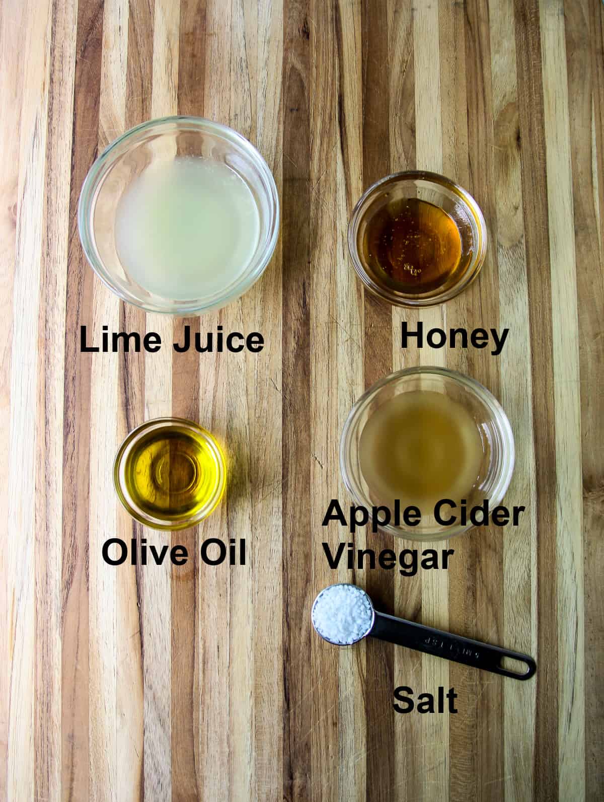 The salad dressing ingredients in glass bowls on a wooden board.