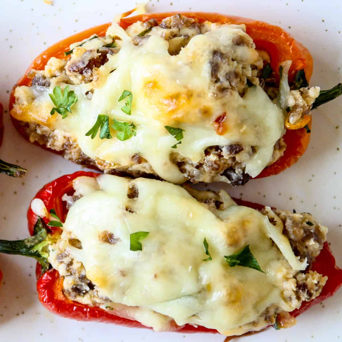 Two sausage stuffed mini peppers on a white plate.