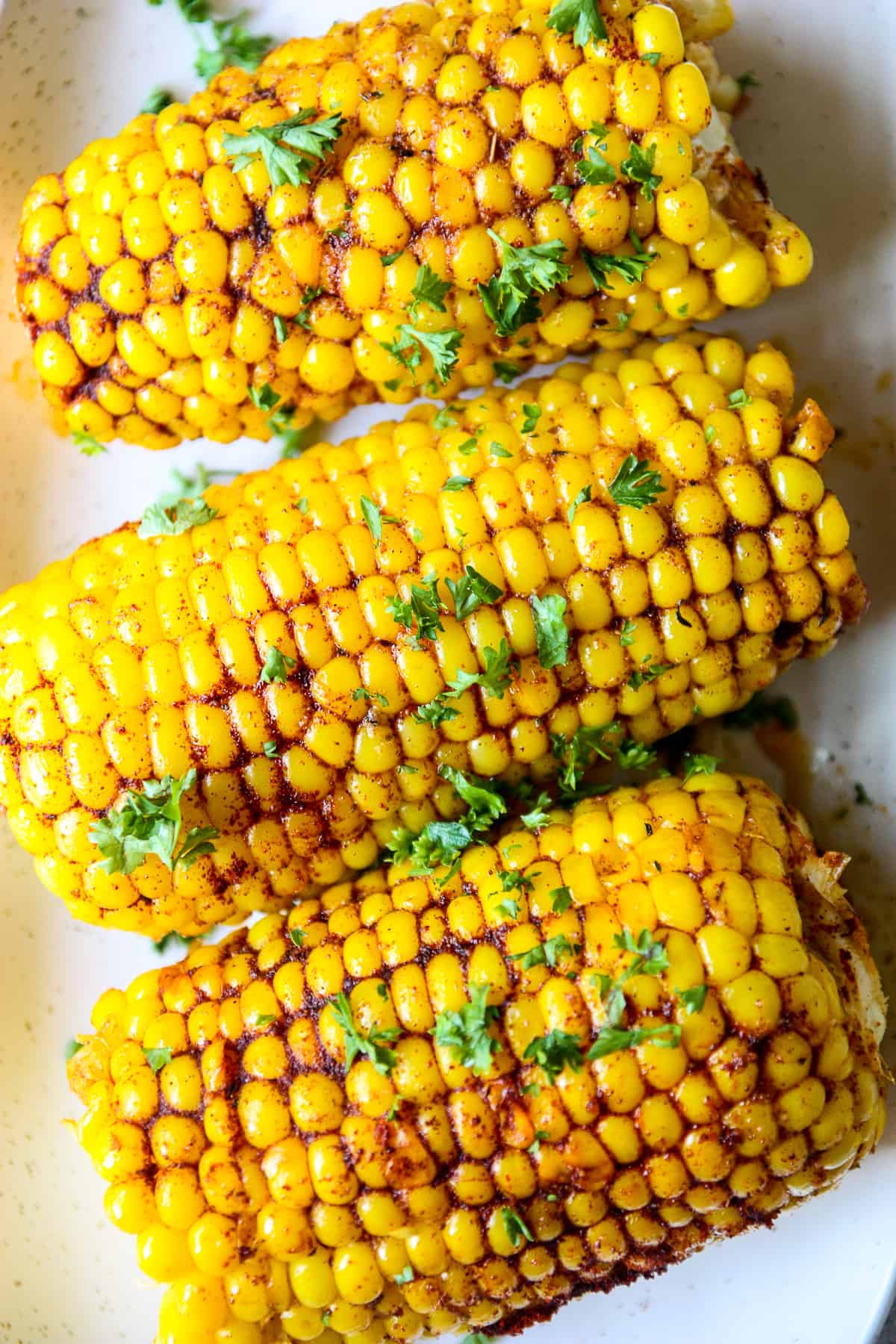 Three ears of Cajun corn on the cob, garnished with parsley.
