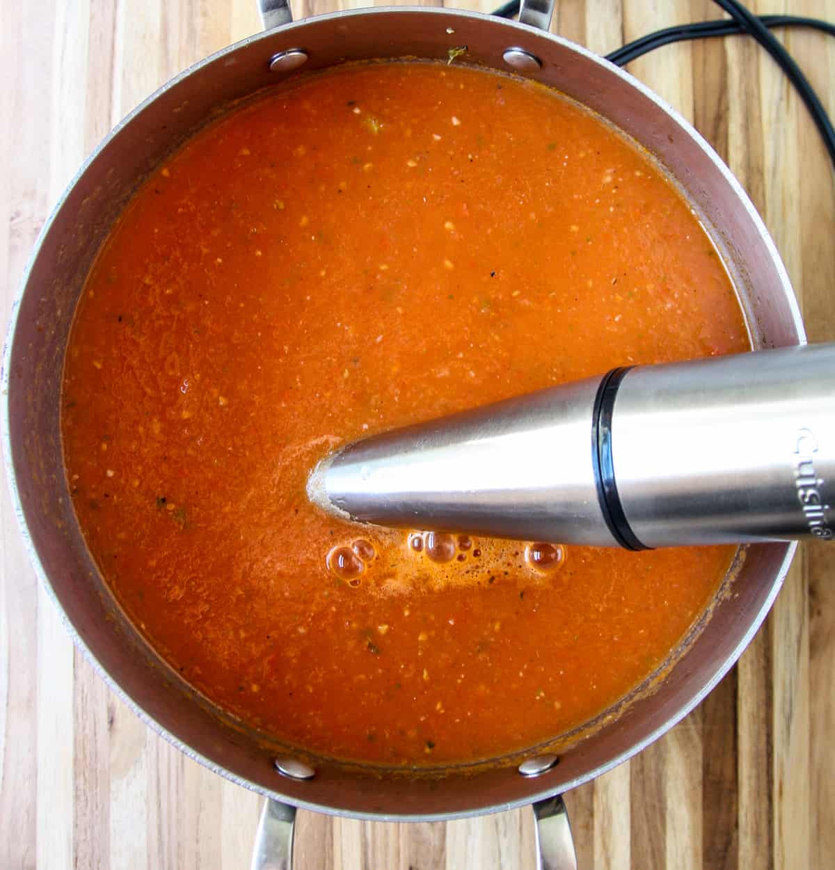 A pot of soup being pureed with an immersion blender.