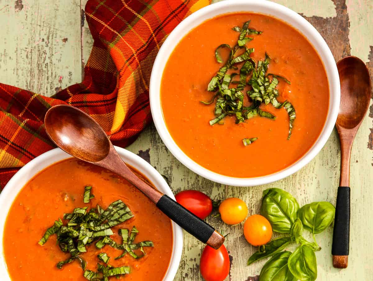 Two white bowls of roasted tomato basil soup with wooden soup spoons.