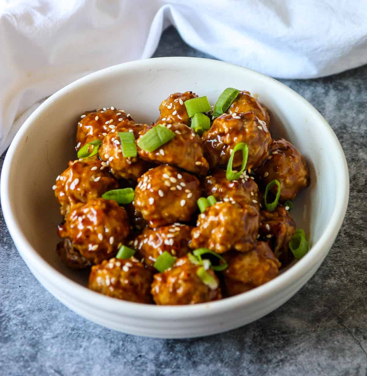 A bowl of baked and glazed Asian chicken meatballs on a marble countertop.
