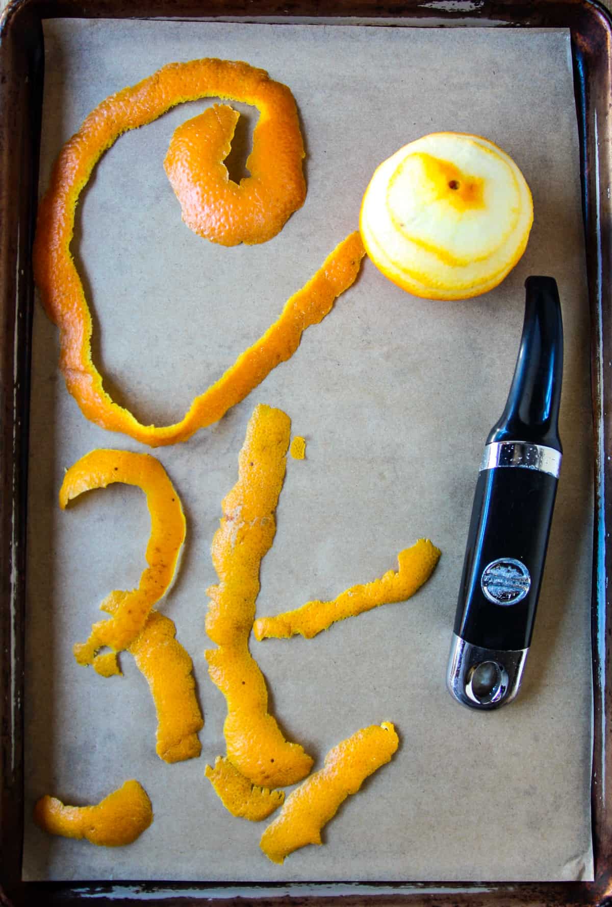 An orange in the process of getting peeled, on a baking tray.