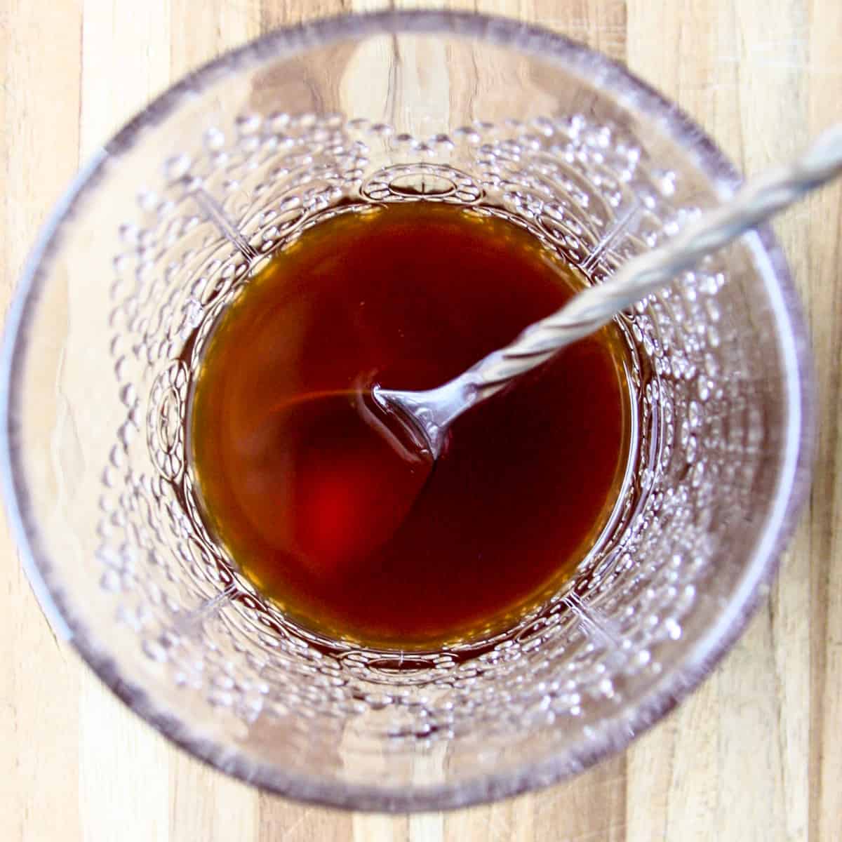 Cocktail ingredients in a glass being stirred with a bar spoon.