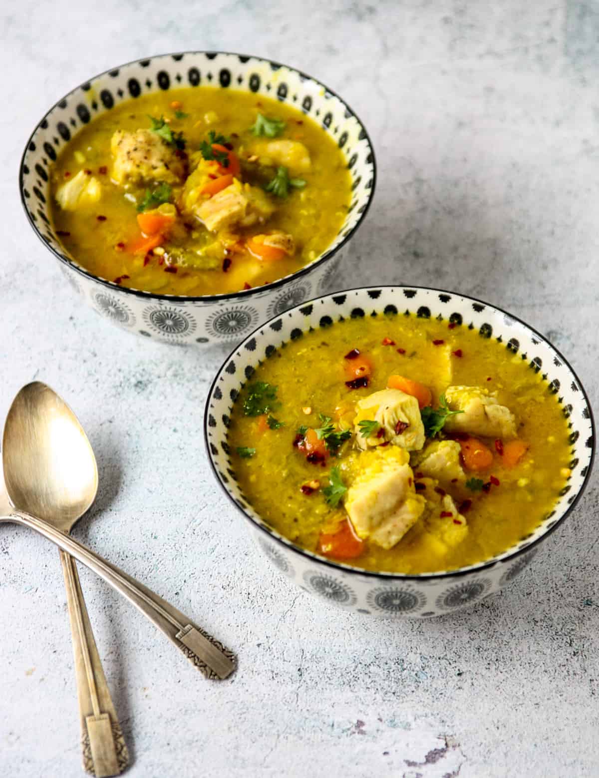 Two bowls of lentil and turkey soup on a marble counter top with two silver spoons.