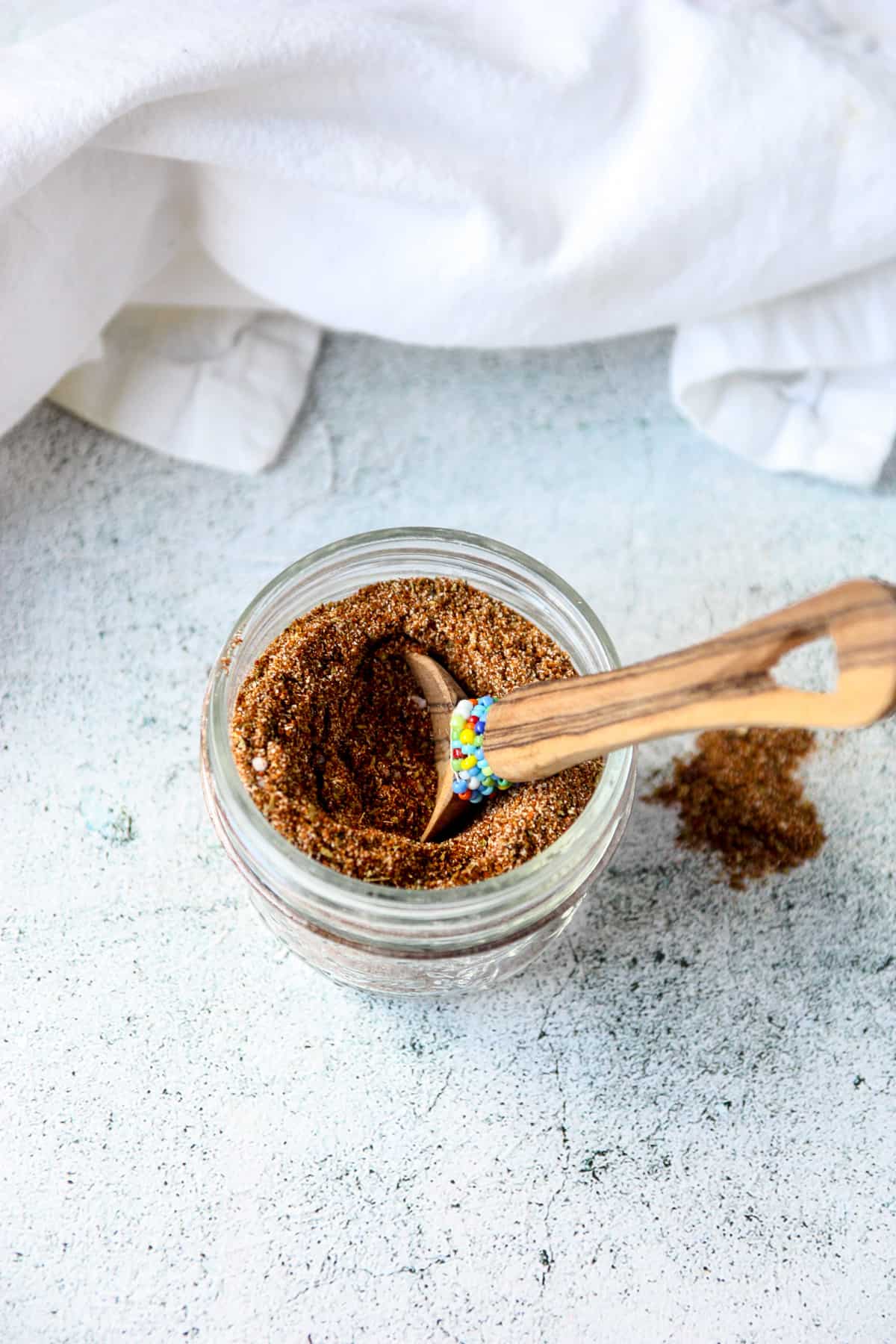 A small wooden spoon inserted into a jar of chicken taco seasoning mix.