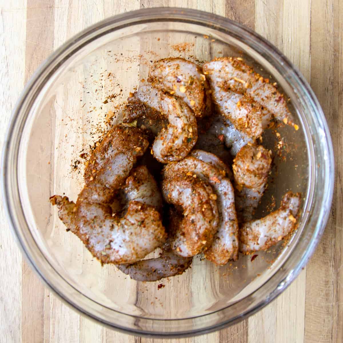 Raw shrimp coated with seasoning, in a glass bowl.
