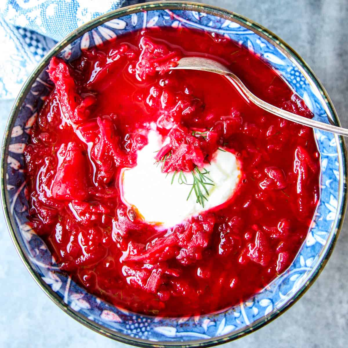 Bright red beet and cabbage soup in a blue and white bowl.