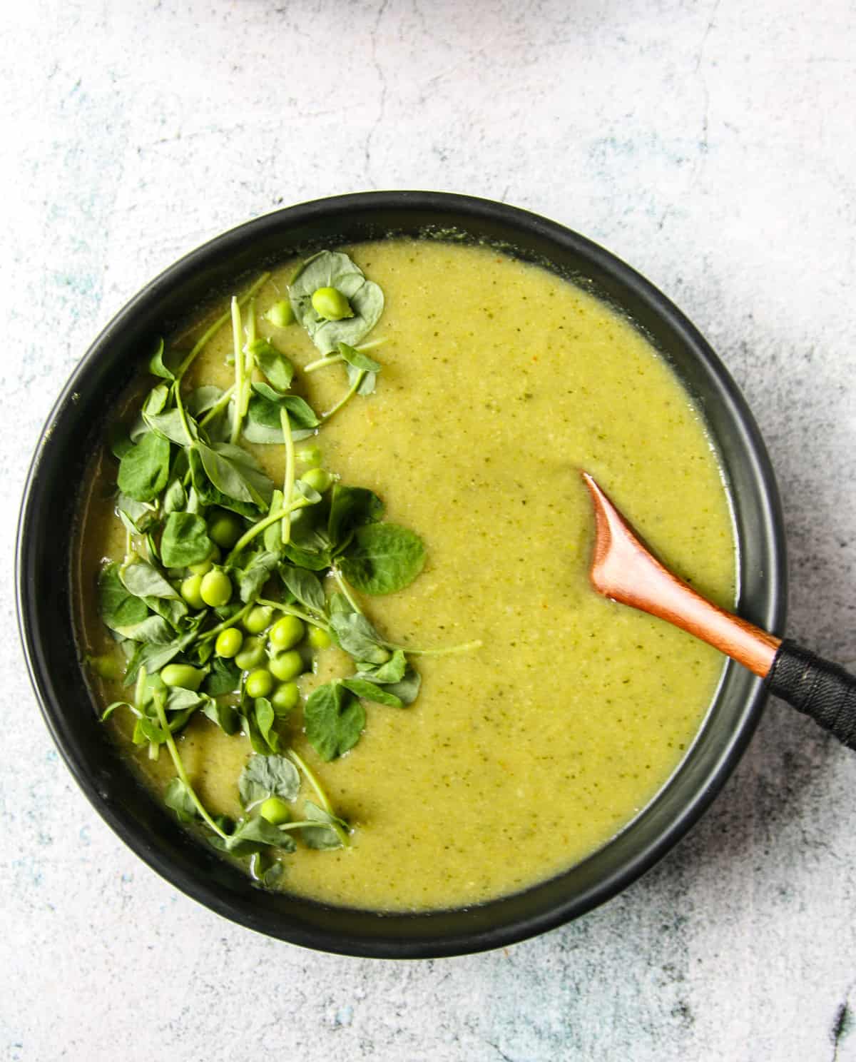 Broccoli and pea soup, garnished with pea shoots and fresh peas.