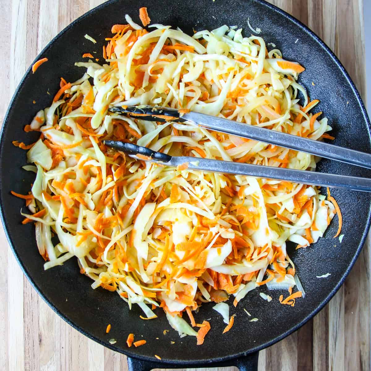 Stir fried cabbage in a cast iron wok with tongs.
