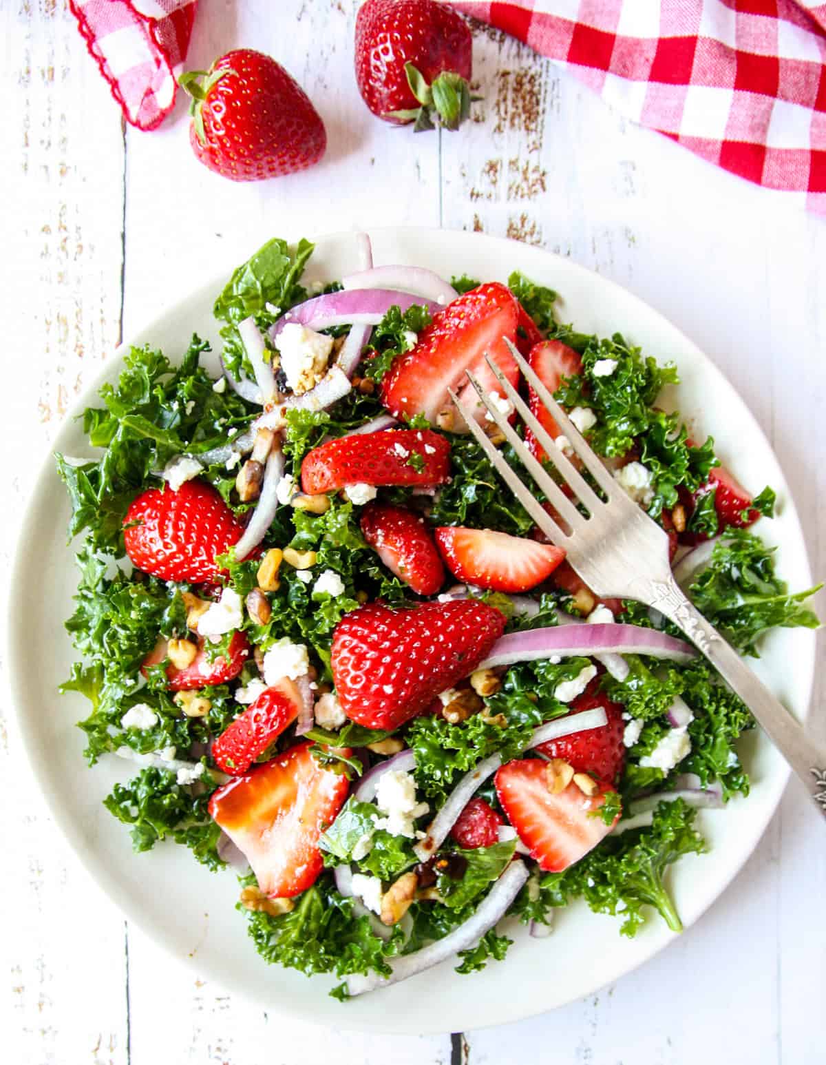 Strawberry kale salad with feta cheese crumbles on a plate with a silver fork.