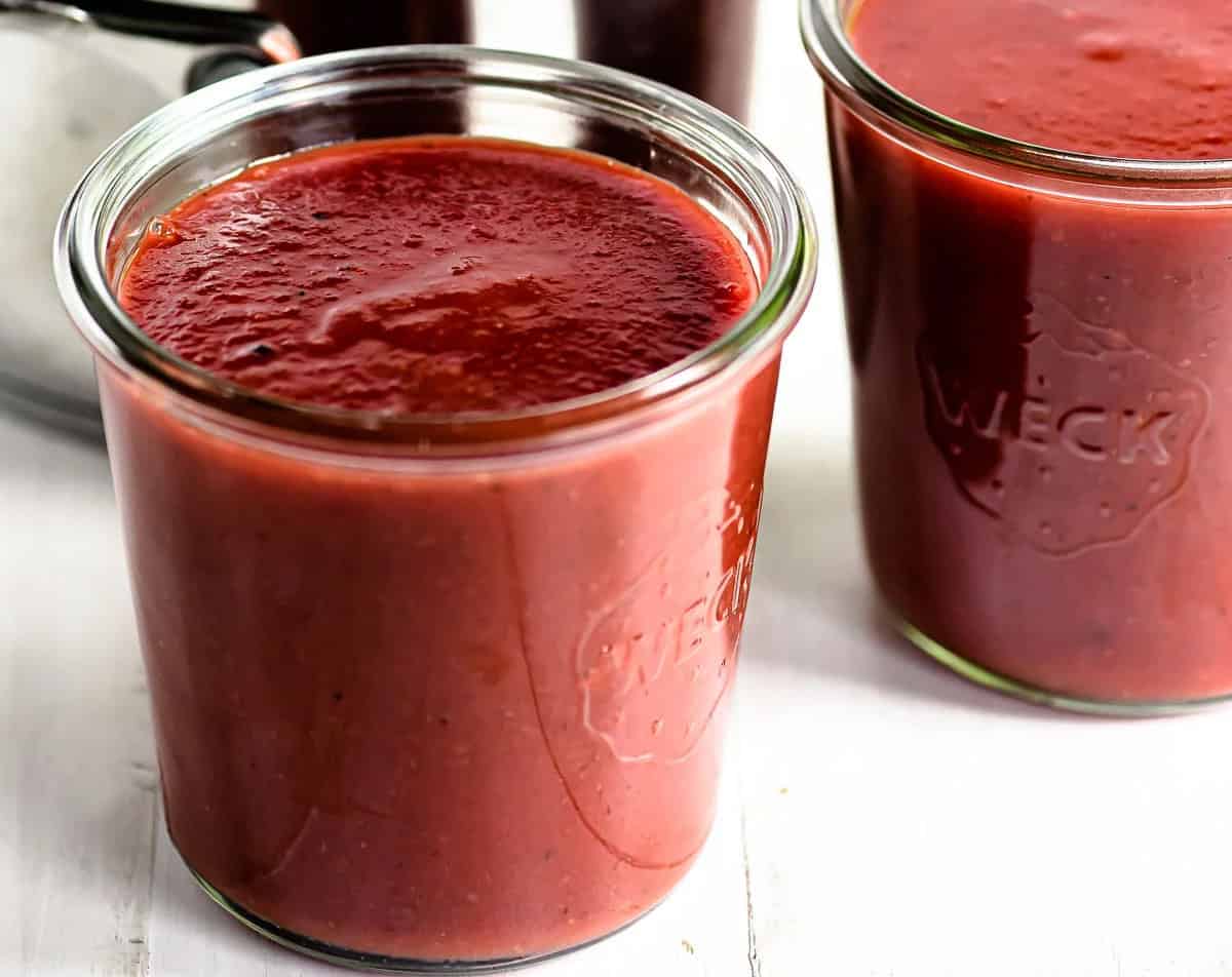 Two glass jars of strawberry barbecue sauce.
