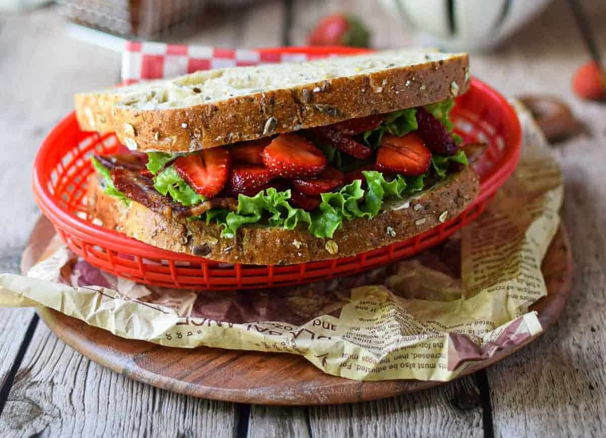 A sandwich with bacon, lettuce, and strawberries on whole wheat bread.
