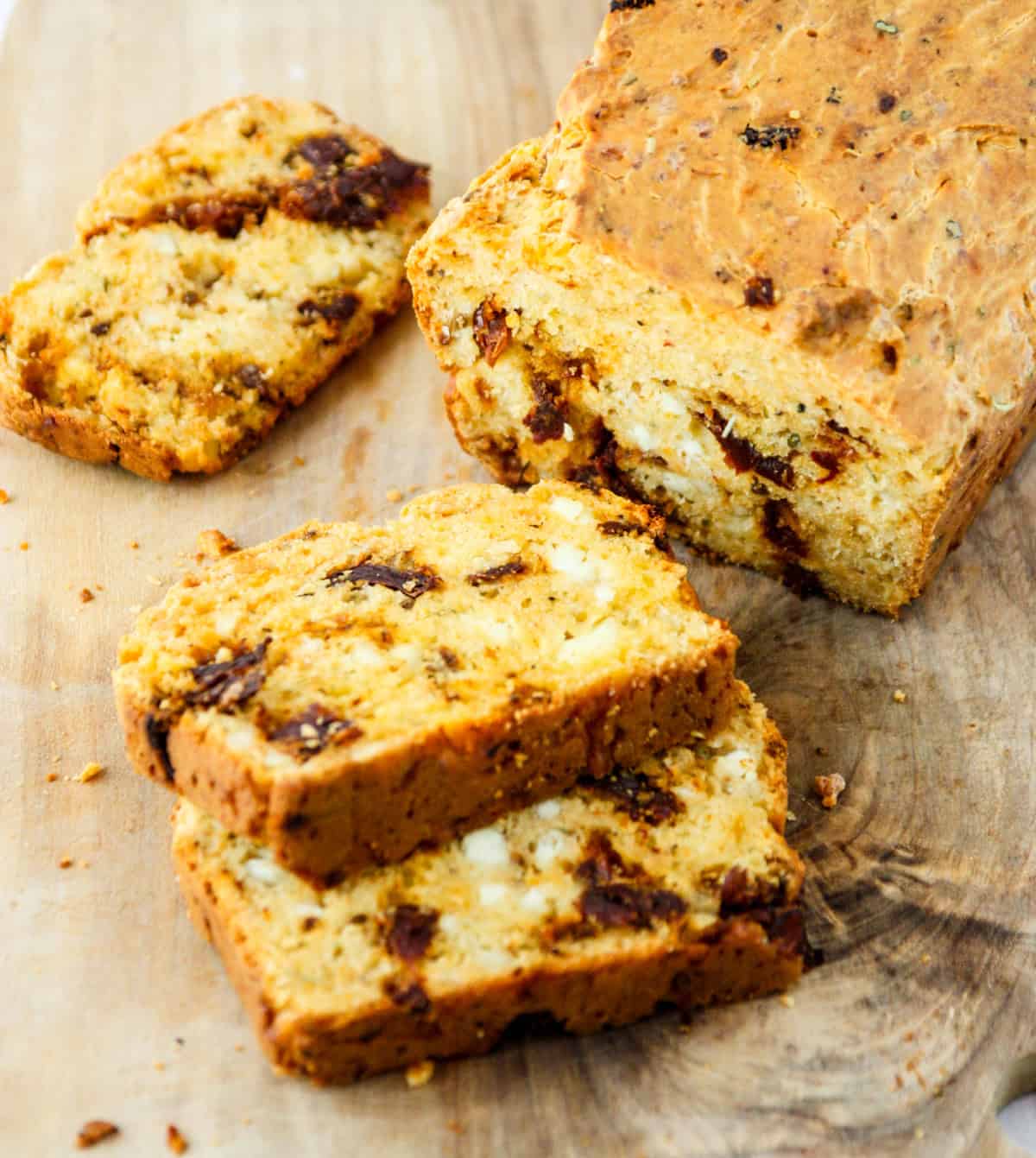 A loaf of sun-dried tomato bread, with three cut slices on a cutting board.
