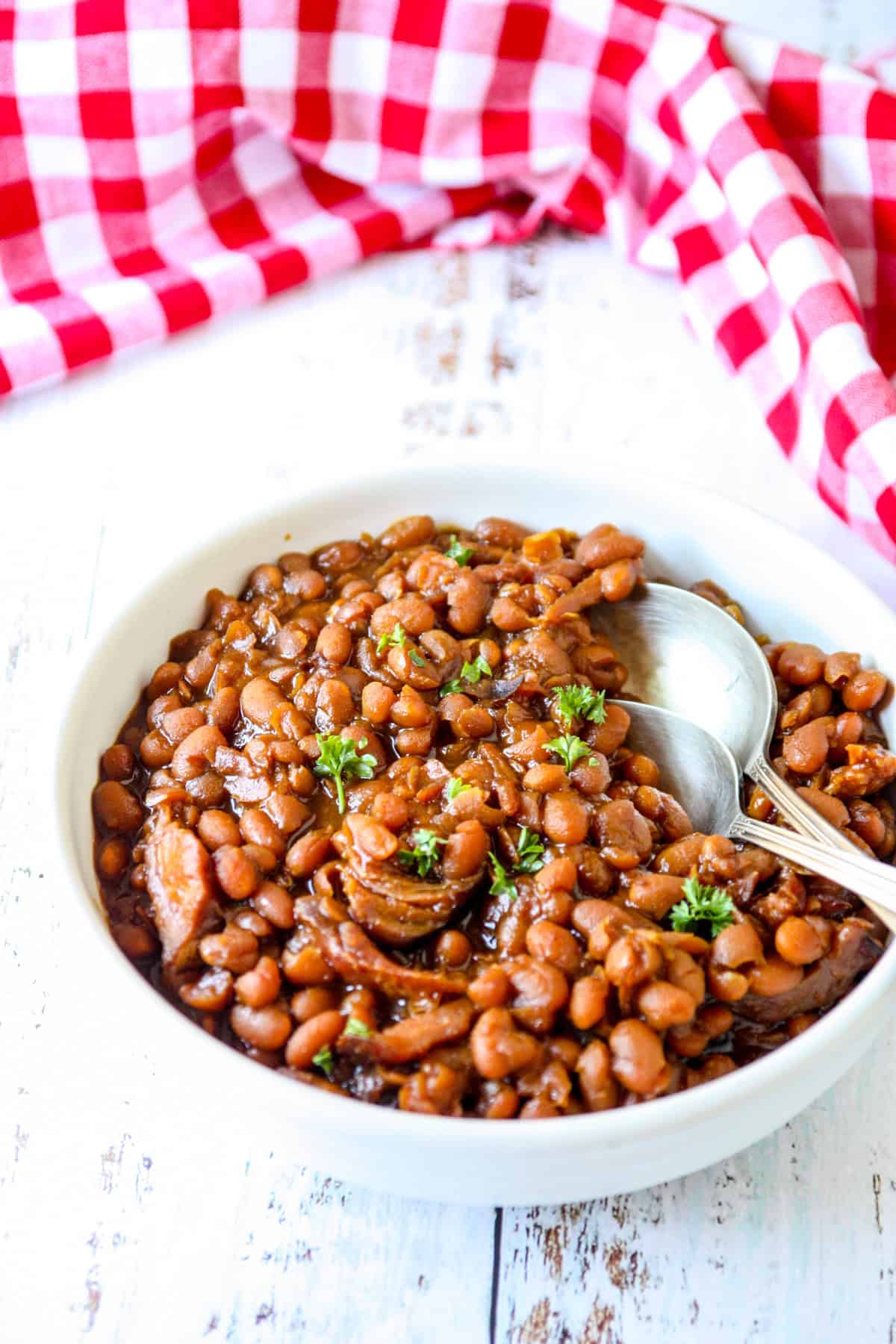Slow cooker baked beans in a white bowl with two spoons.