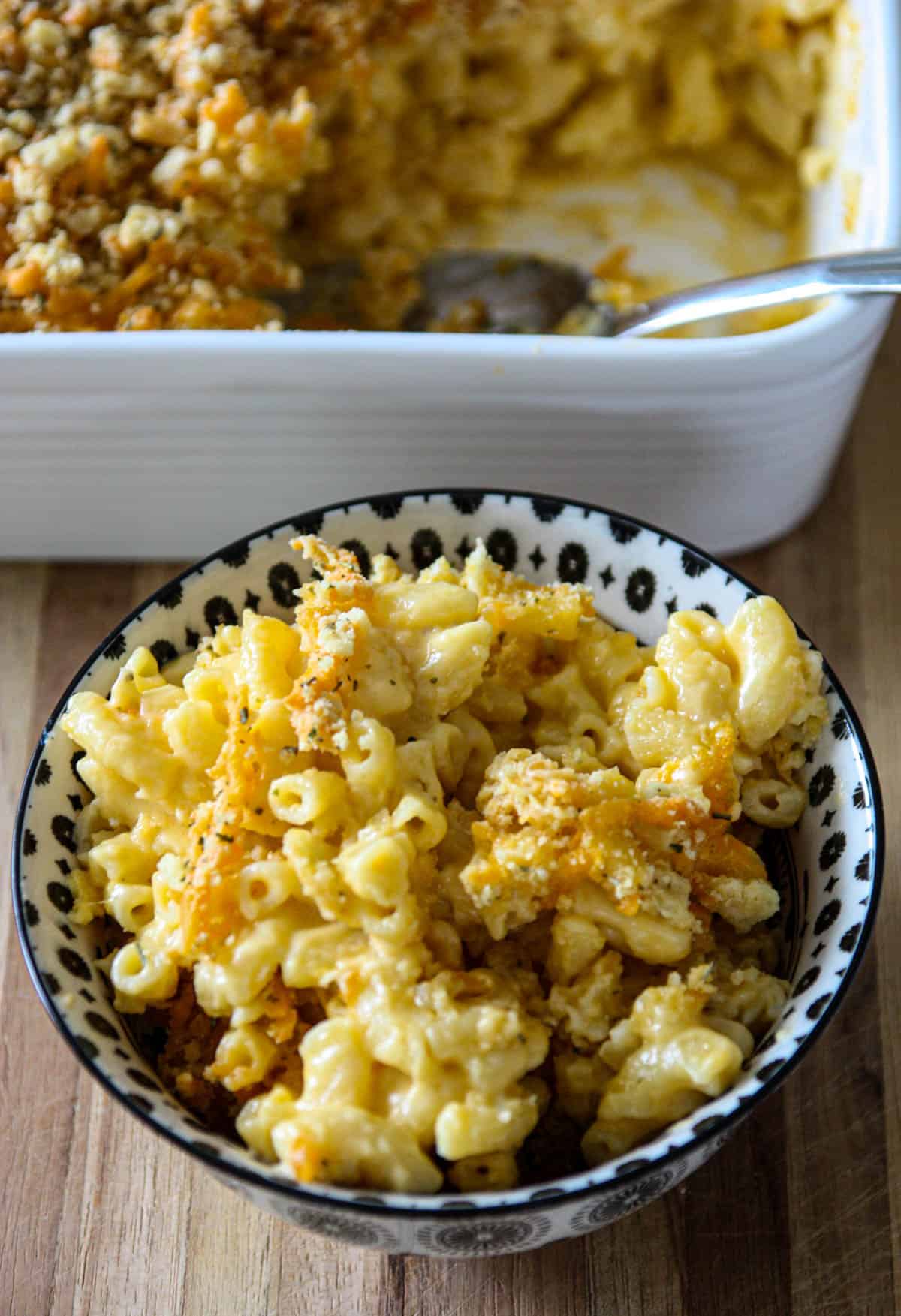 A bowl of old fashioned baked macaroni and cheese next to a casserole dish.