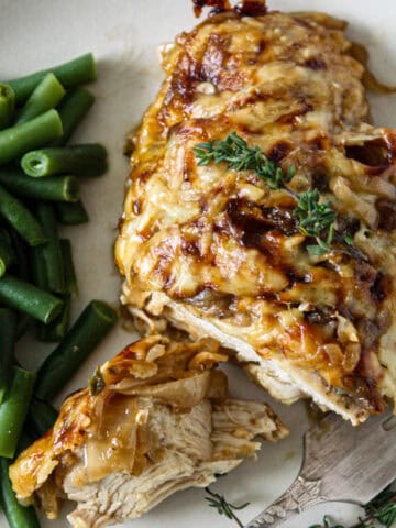 French onion chicken on a white plate with green beans.