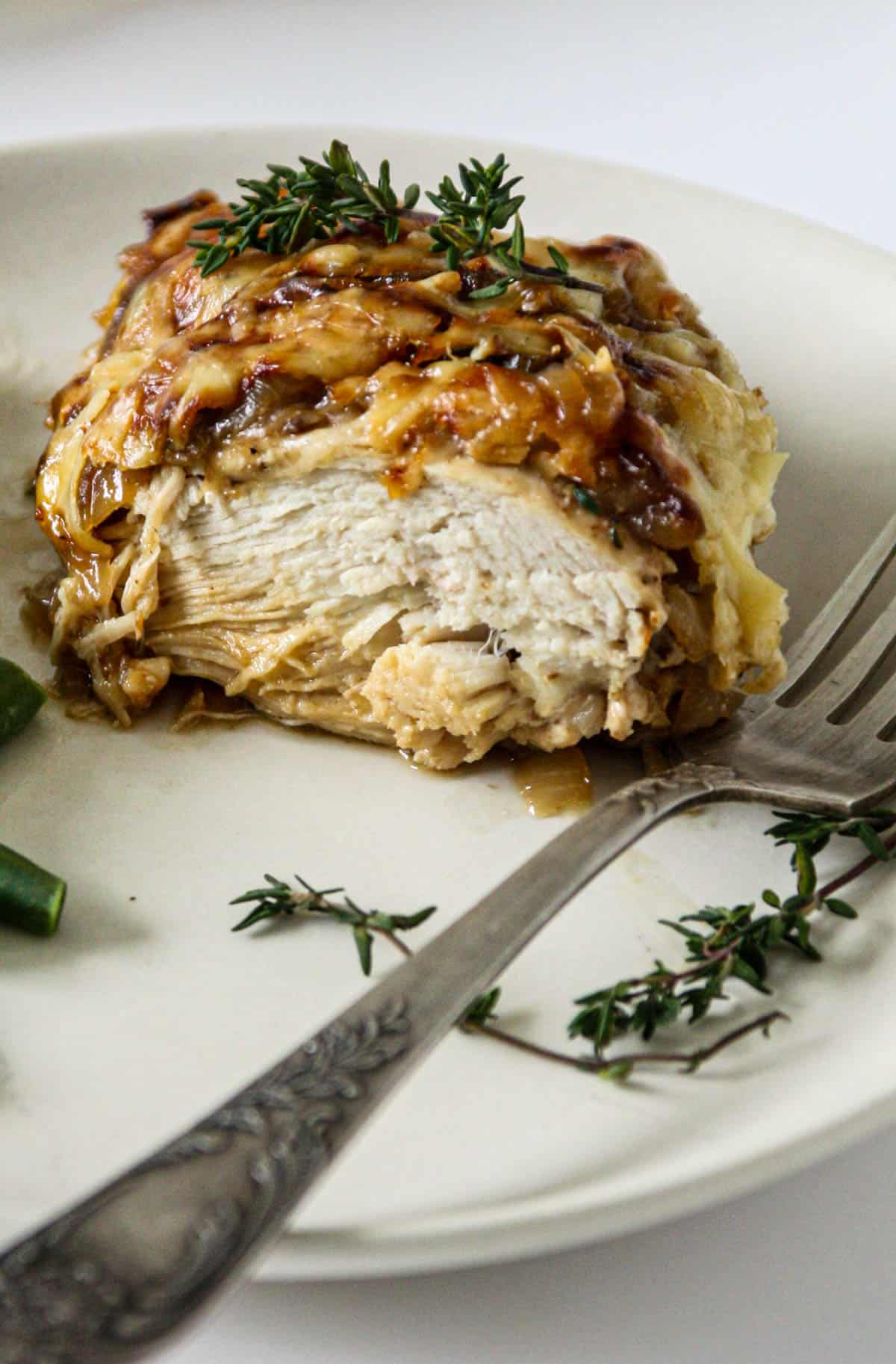 French onion chicken on a white plate, garnished with a sprig of thyme.