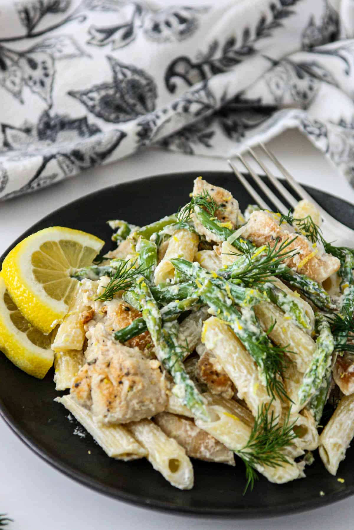 A plate full of pasta with asparagus and chicken with a fork.