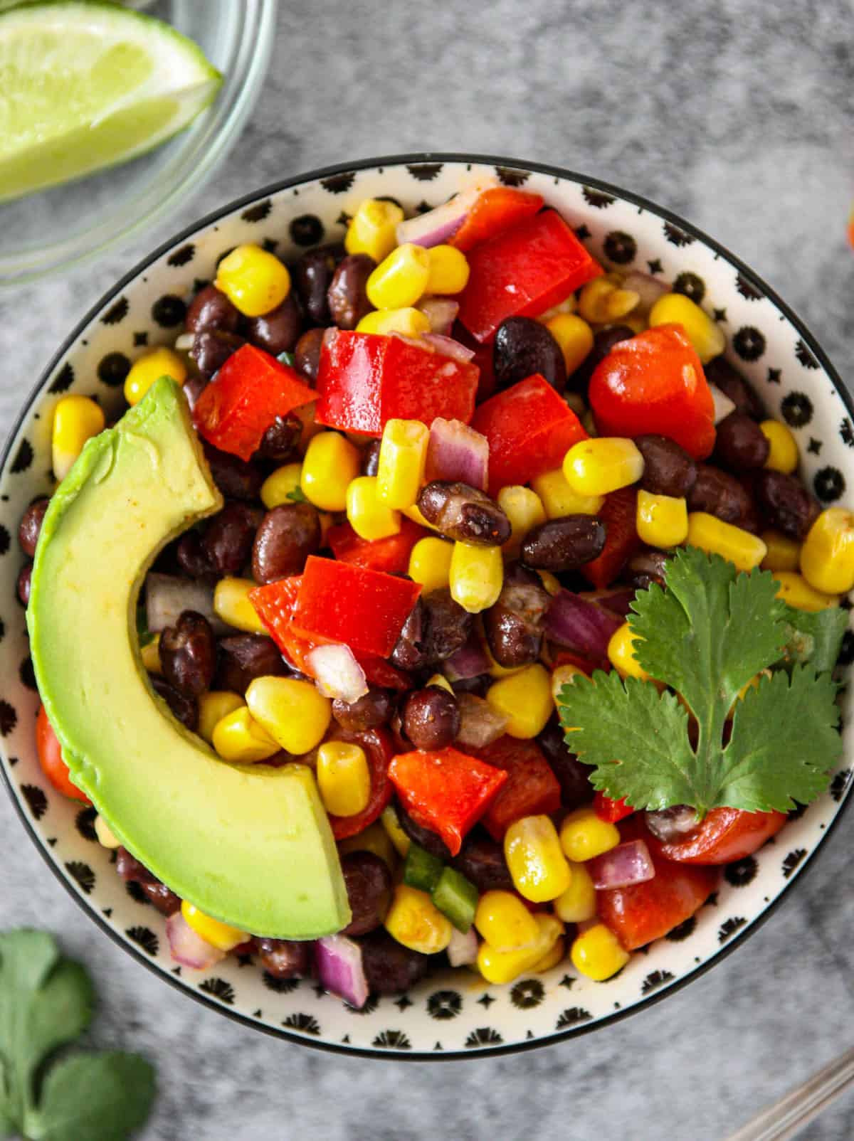 Corn and black bean salad topped with avocado slices in a black and white dish.