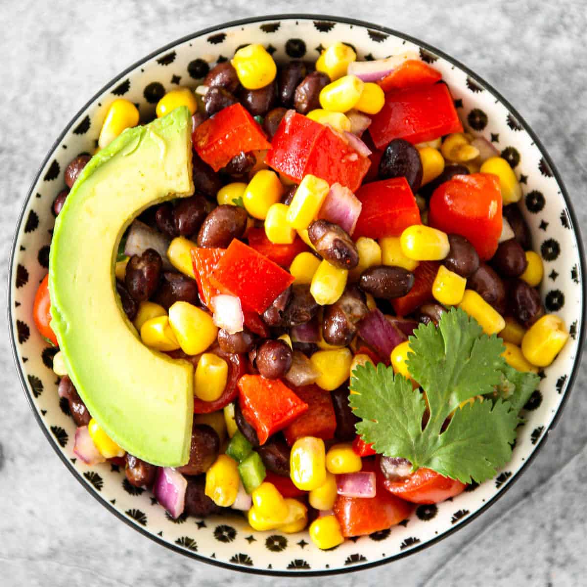 Fiesta salad topped with avocado slices, in a black and white bowl.
