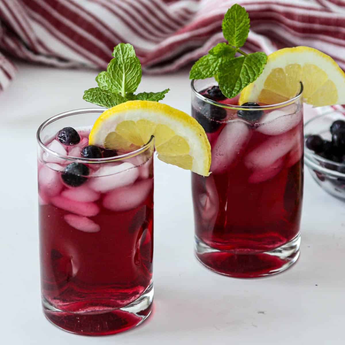Two glasses of blueberry iced tea, garnished with lemon slices.