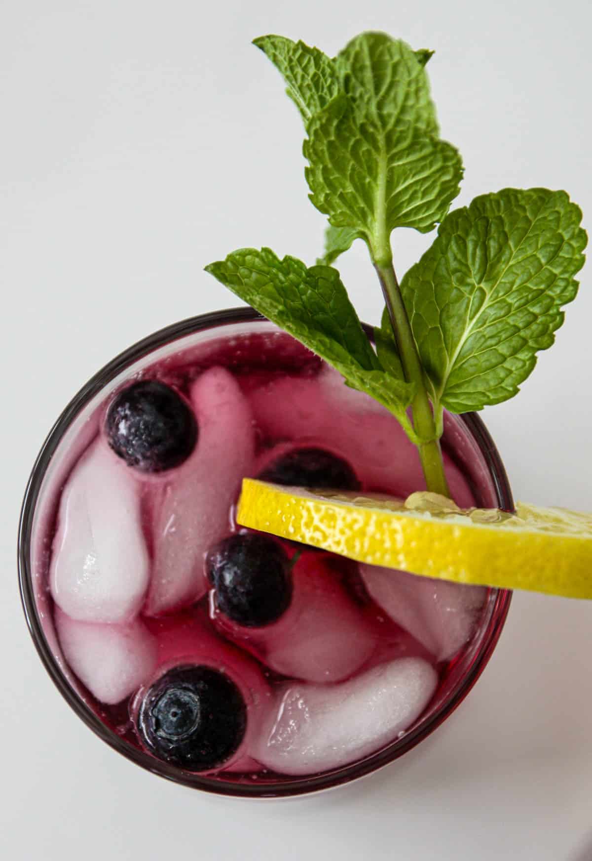 Blueberry iced tea in a glass with ice and a lemon slice.