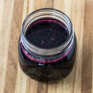 A glass jar of blueberry simple syrup on a wooden board.