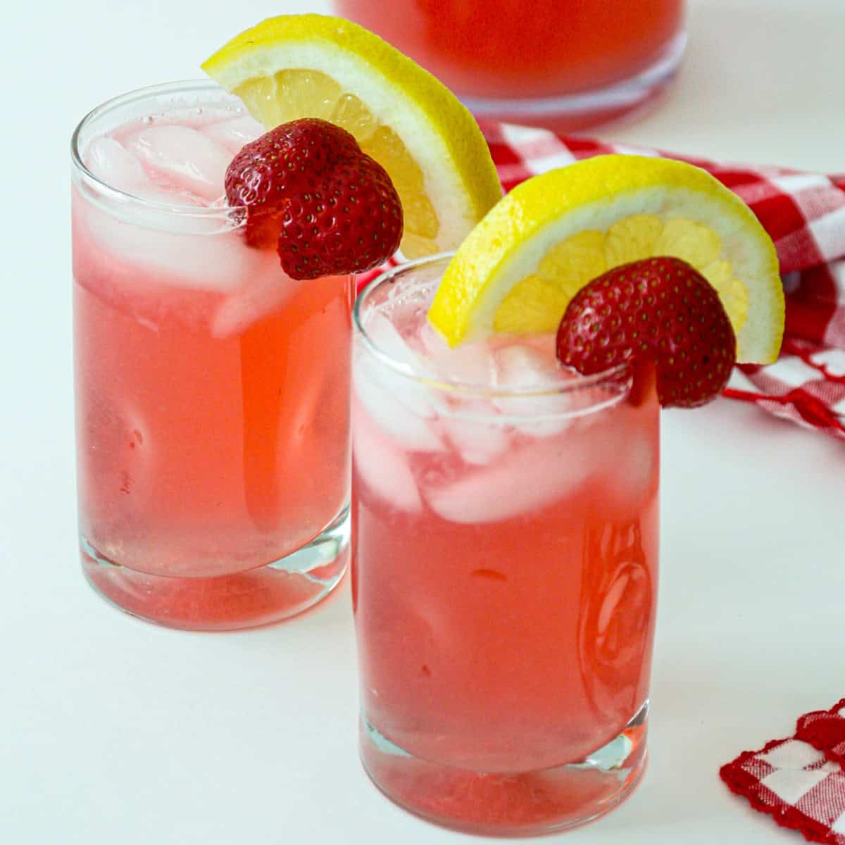 Two glasses of rhubarb lemonade, garnished with lemon slices and strawberries.
