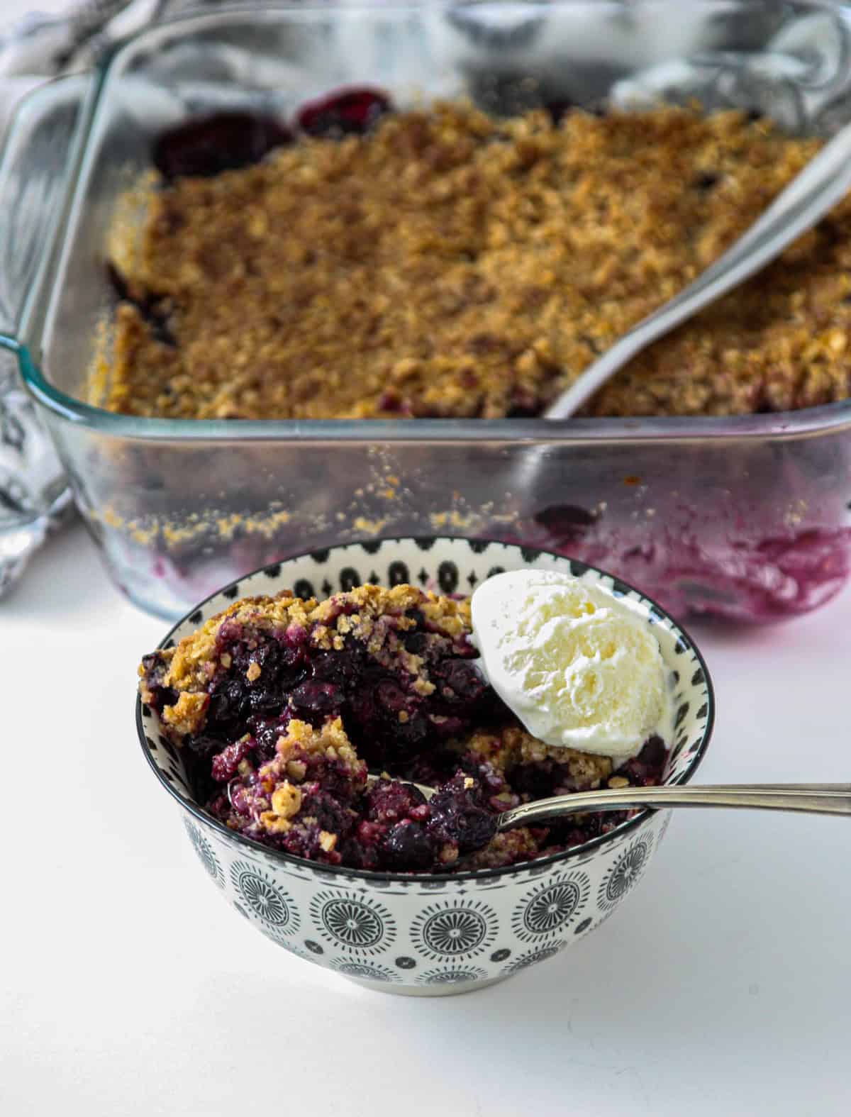 A serving of gluten free blueberry crisp in a bowl with a silver spoon inserted.