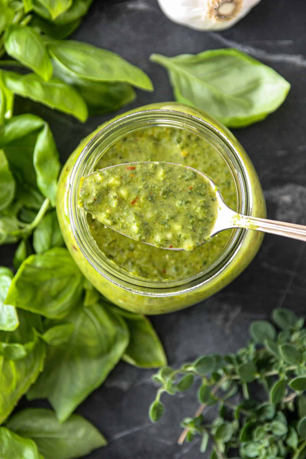 A spoonful of basil chimichurri sauce over a glass jar of sauce.