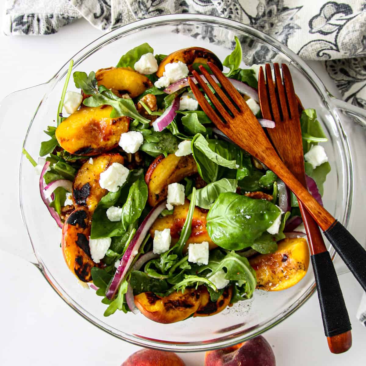 Grilled peach salad in a glass bowl with two wooden forks.